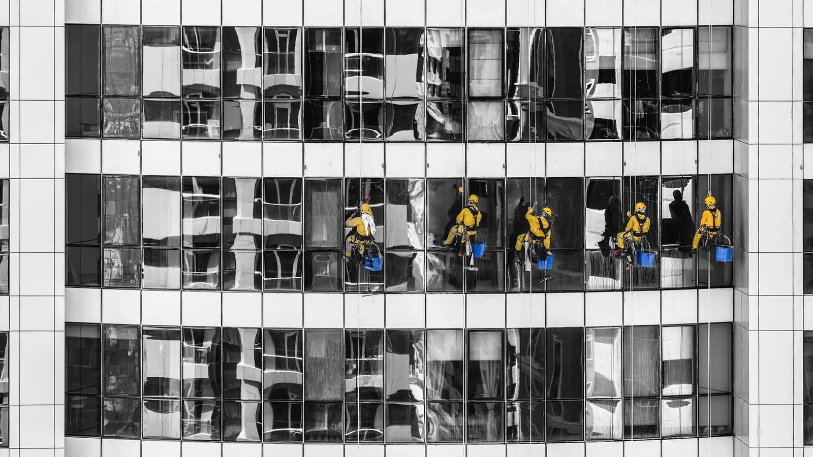 Five professional window cleaners suspended across a commercial glass building